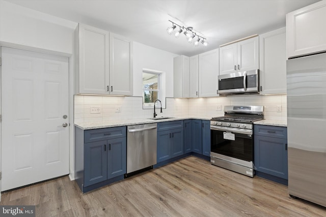 kitchen with light wood finished floors, tasteful backsplash, blue cabinetry, appliances with stainless steel finishes, and a sink