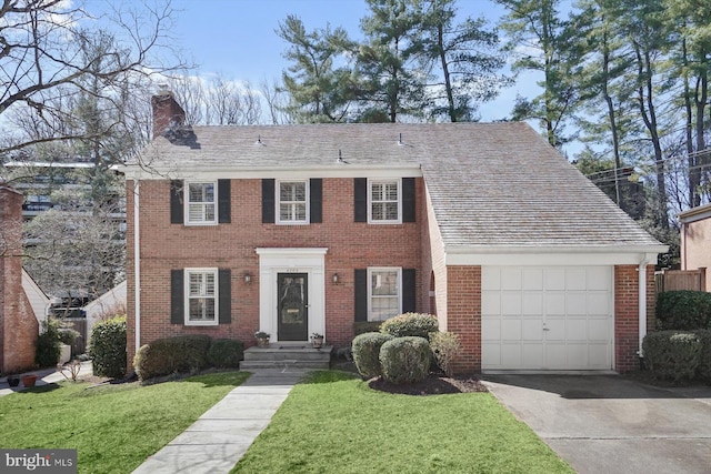 colonial home with brick siding, an attached garage, a chimney, and a front lawn