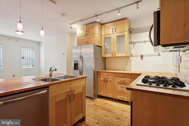 kitchen featuring butcher block counters, light wood-style flooring, appliances with stainless steel finishes, hanging light fixtures, and a sink