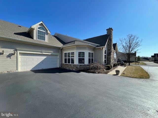 view of side of home with aphalt driveway, an attached garage, and stone siding