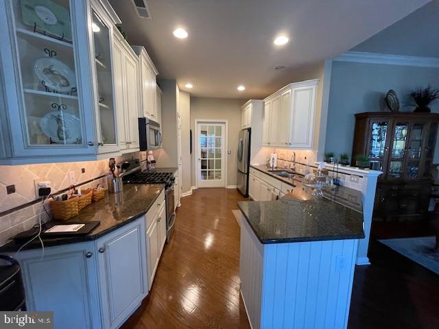 kitchen with visible vents, glass insert cabinets, a peninsula, stainless steel appliances, and dark wood-style flooring