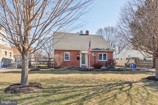 view of front facade with fence, a front yard, a shingled roof, brick siding, and a chimney