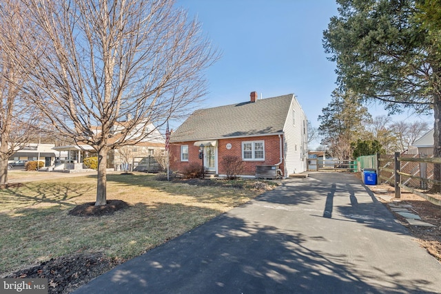 view of front facade featuring brick siding, fence, aphalt driveway, entry steps, and a chimney