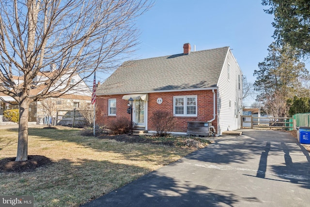 view of front facade with a front yard, brick siding, a chimney, and fence