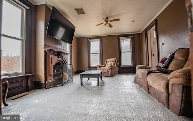 living area featuring a ceiling fan, a fireplace, visible vents, and ornamental molding