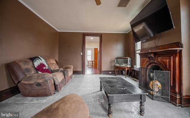 living area featuring visible vents, baseboards, a fireplace with raised hearth, and crown molding