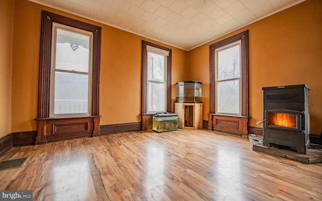 unfurnished living room featuring visible vents, crown molding, a wood stove, and wood finished floors