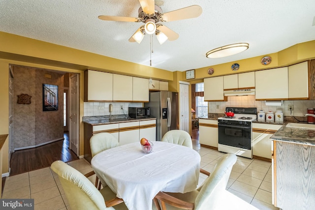 kitchen featuring under cabinet range hood, stainless steel appliances, dark countertops, and light tile patterned flooring