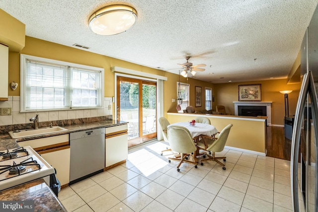 kitchen featuring light tile patterned floors, visible vents, a fireplace, a sink, and appliances with stainless steel finishes