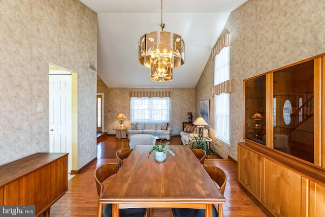 dining space featuring wallpapered walls, high vaulted ceiling, an inviting chandelier, and wood finished floors