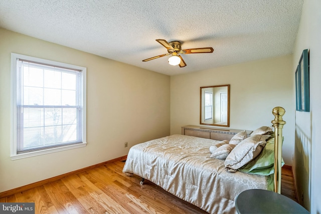 bedroom featuring light wood-style flooring, a ceiling fan, baseboards, and a textured ceiling