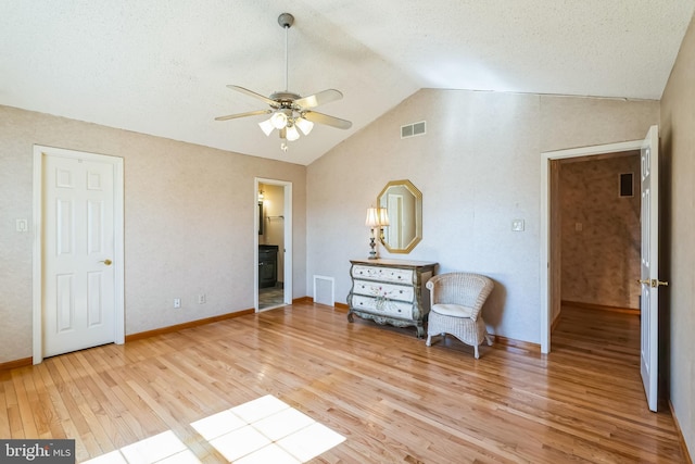 living area featuring a ceiling fan, lofted ceiling, light wood-style floors, and visible vents