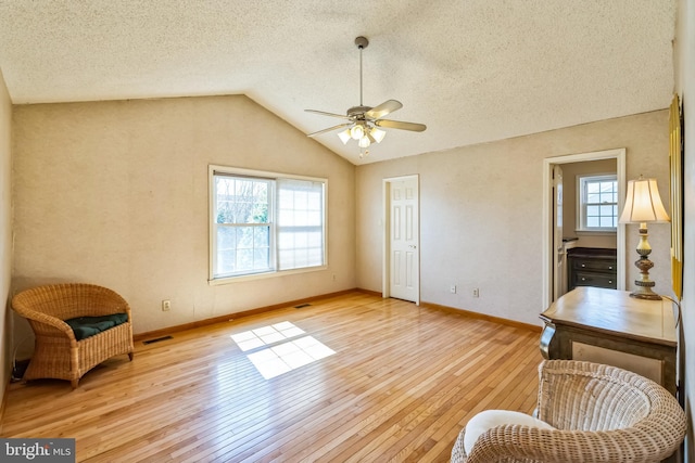 sitting room with baseboards, visible vents, light wood finished floors, vaulted ceiling, and a textured ceiling