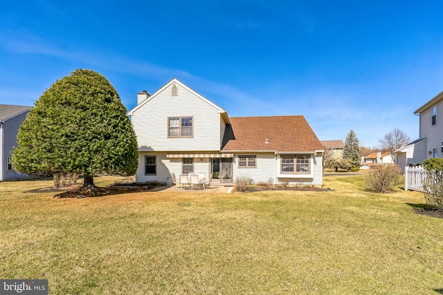 rear view of property featuring a yard, a patio, a chimney, and a shingled roof