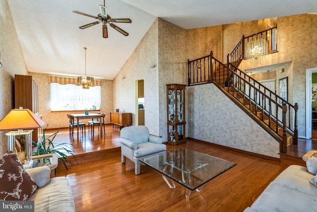 living area featuring wallpapered walls, baseboards, stairs, wood finished floors, and high vaulted ceiling