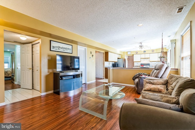 living area with baseboards, visible vents, light wood-type flooring, and a textured ceiling