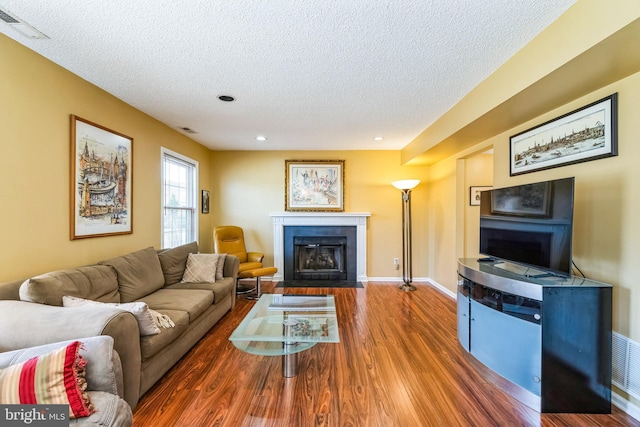 living area with wood finished floors, baseboards, visible vents, a fireplace with flush hearth, and a textured ceiling