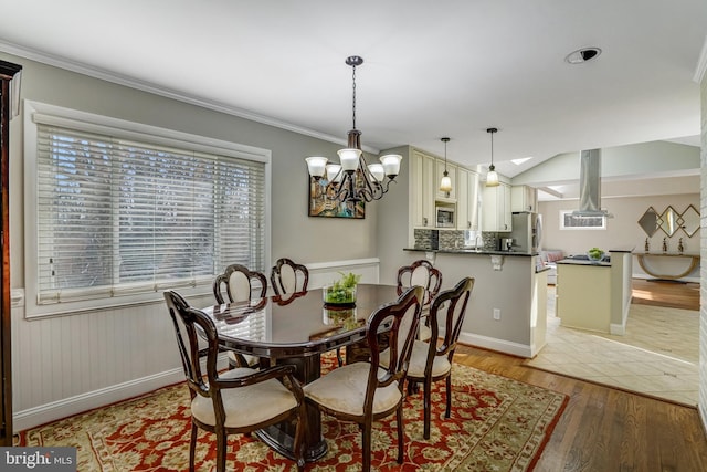 dining space with a notable chandelier, light wood-style floors, wainscoting, and crown molding