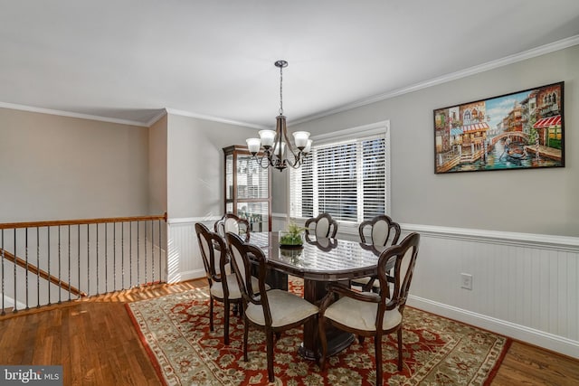 dining room with a wainscoted wall, wood finished floors, a chandelier, and ornamental molding