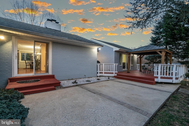 exterior space with brick siding, a wooden deck, a gazebo, a chimney, and a patio