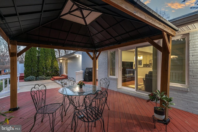 deck at dusk with a gazebo, outdoor dining space, and area for grilling