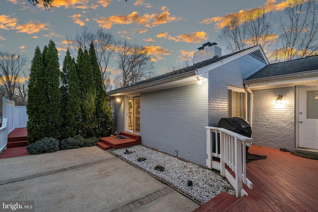 view of side of home featuring a deck, a patio area, brick siding, and a chimney