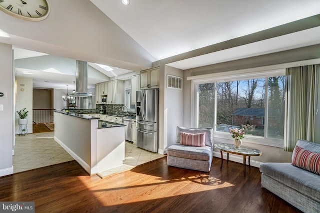 kitchen with visible vents, lofted ceiling with skylight, a sink, appliances with stainless steel finishes, and island range hood