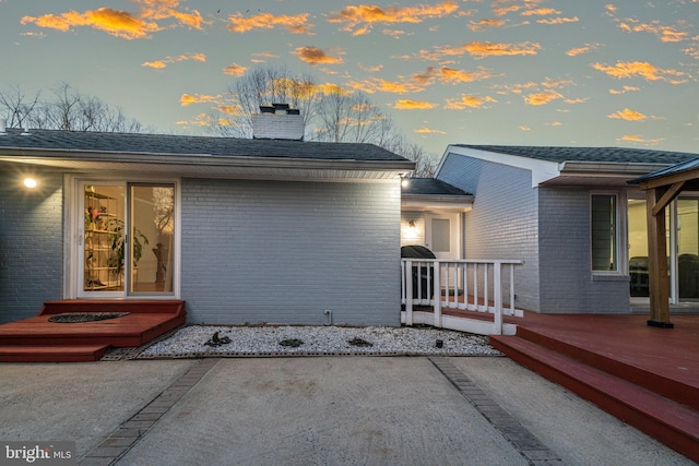 exterior space with brick siding, a patio, a chimney, and a deck