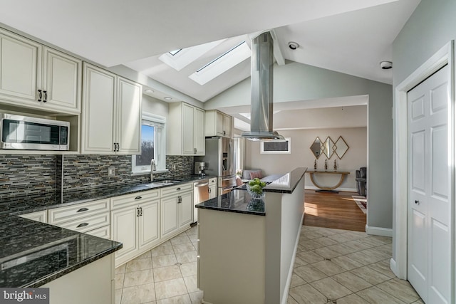 kitchen with a sink, stainless steel appliances, lofted ceiling with skylight, and dark stone counters