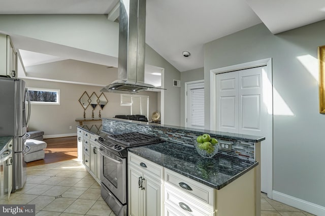 kitchen with lofted ceiling, dark stone counters, light tile patterned flooring, appliances with stainless steel finishes, and island range hood