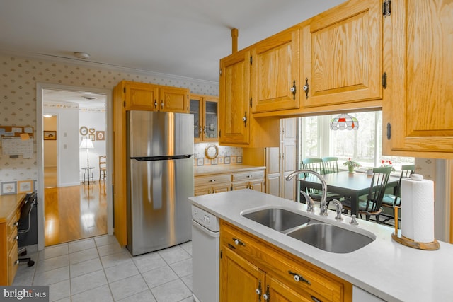 kitchen with wallpapered walls, light countertops, freestanding refrigerator, and a sink