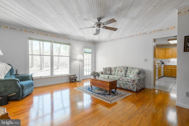 living room featuring baseboards, light wood-type flooring, and ceiling fan