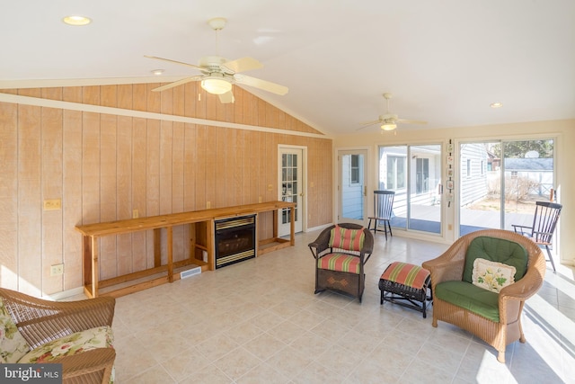 living room featuring wooden walls, a ceiling fan, light tile patterned flooring, a sunroom, and vaulted ceiling