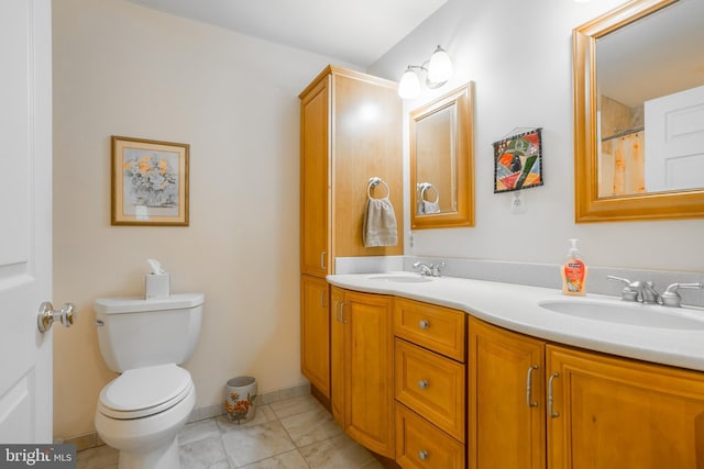 bathroom featuring double vanity, toilet, baseboards, and a sink