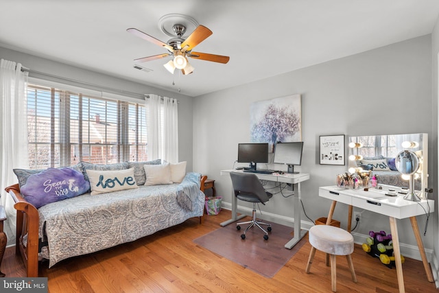 office area with ceiling fan, visible vents, baseboards, and wood finished floors