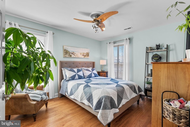 bedroom featuring ceiling fan, visible vents, multiple windows, and wood finished floors