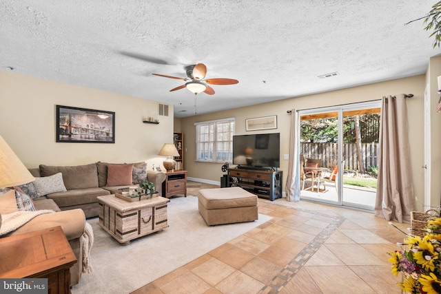 living area with a textured ceiling, baseboards, visible vents, and ceiling fan