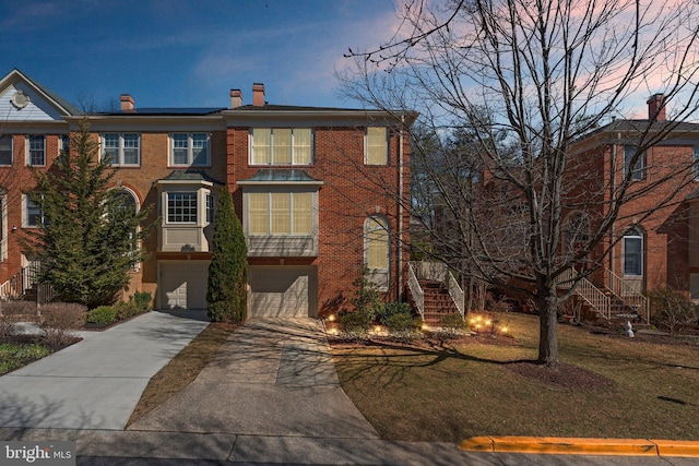 view of front facade with driveway, stairs, a garage, brick siding, and a chimney