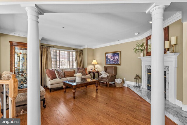 living room with wood finished floors, baseboards, ornate columns, a high end fireplace, and ornamental molding