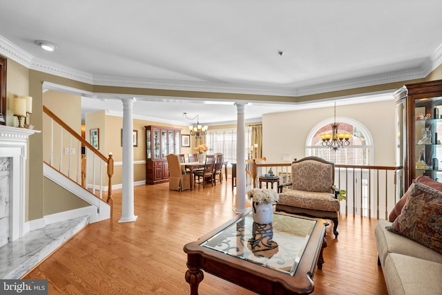 living area featuring light wood-type flooring, an inviting chandelier, crown molding, and ornate columns