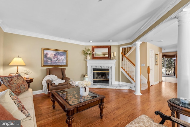 living area with a premium fireplace, decorative columns, wood finished floors, and stairs