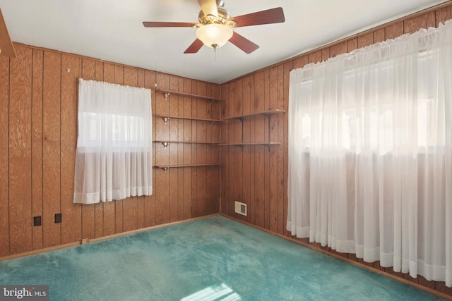 carpeted spare room featuring visible vents, ceiling fan, and wooden walls