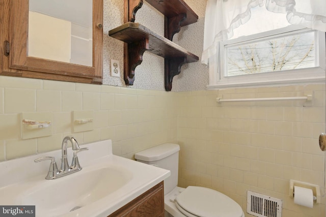 bathroom with vanity, a wainscoted wall, visible vents, wallpapered walls, and toilet