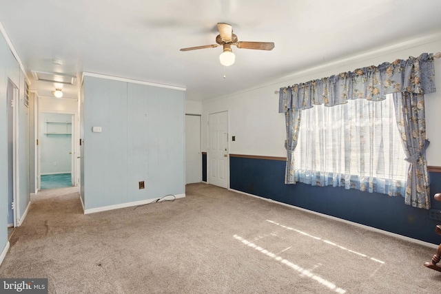 carpeted empty room featuring baseboards, attic access, ceiling fan, and ornamental molding