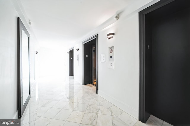 corridor featuring elevator, marble finish floor, and baseboards