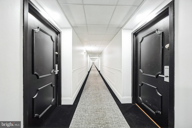 hallway featuring a drop ceiling, wainscoting, and a decorative wall