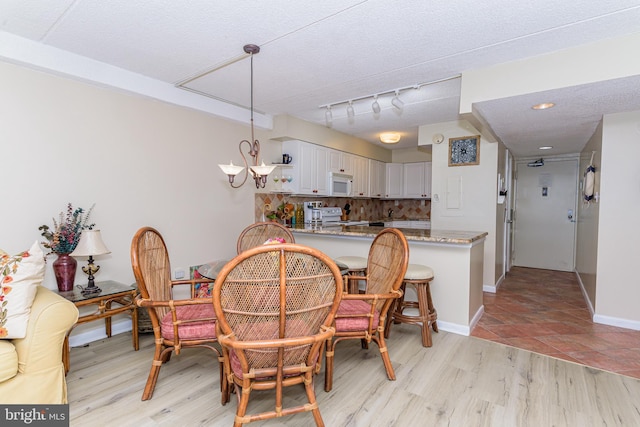 dining area featuring a textured ceiling, baseboards, a notable chandelier, and light wood finished floors