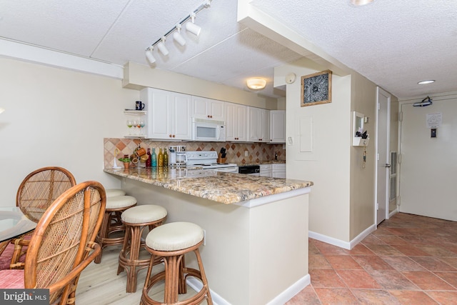 kitchen with a breakfast bar, white appliances, a peninsula, and backsplash