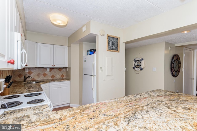 kitchen with tasteful backsplash, light stone counters, white appliances, white cabinetry, and a sink