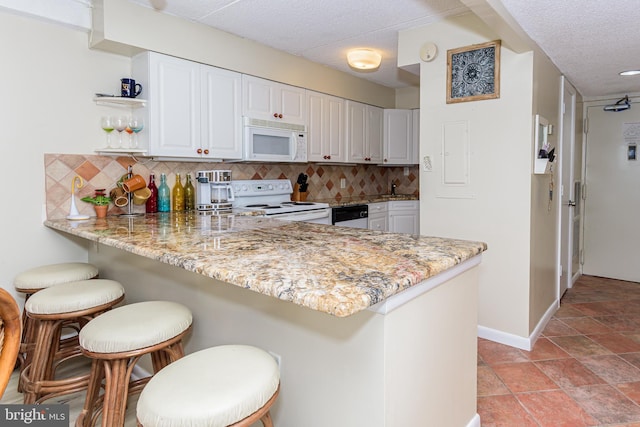 kitchen featuring white appliances, white cabinetry, a peninsula, a kitchen bar, and tasteful backsplash